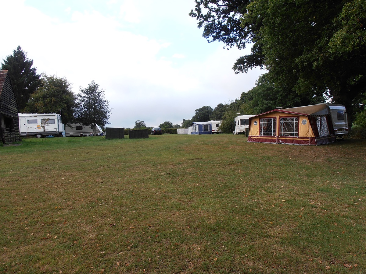 The Certificated Location field at Goffsland Farm, with touring caravans, a motorhome and a drawn-out awning pitched along the edge of the grass beneath mature oak trees